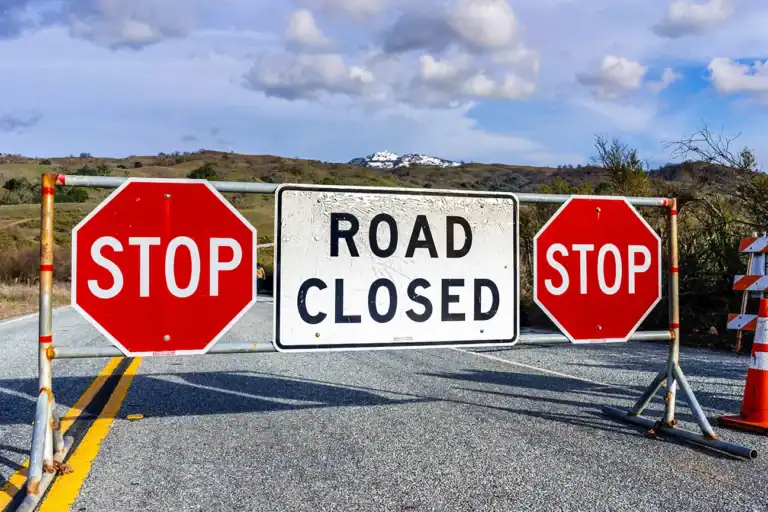 Road Closed sign posted on Mt Hamilton road due to snow, South San Francisco Bay Area, California; snow visible on the summit in the background