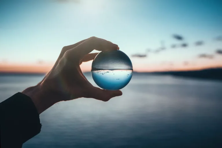 Selective focus to help with mindfulness is shown with a ice cube sphere and a lake and hills in the background.